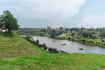 Fototapeta premium Scenic view of the Neman River and green riverside landscape in Grodno, Belarus, with the city skyline in the distance on a sunny summer day.