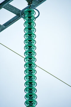 Close-up of green glass disc insulators on a high-voltage power line against an overcast sky.