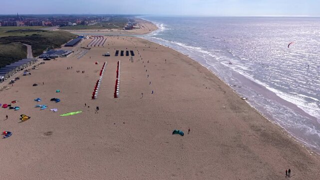 Aerial view video clip of Katwijk aan Zee sandy beach, kitesurfers, beach cabins, coastal dunes, and glistening North Sea waves in South Holland, Netherlands on a sunny day