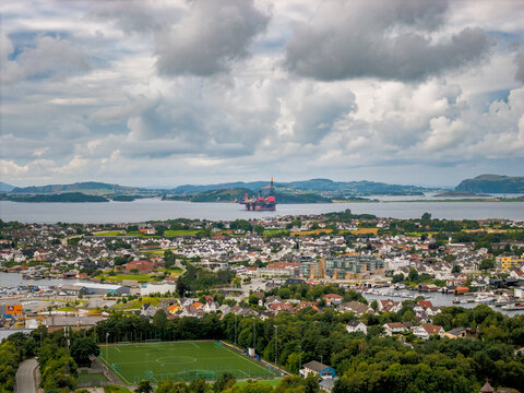 Aerial view of the coastal city of Stavanger with its harbor, a distant oil rig, a green soccer field, and residential areas in Stavanger, Rogaland, Norway.