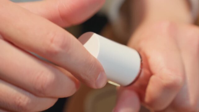 Caucasian artist sampling gloss at cafe, tight closeup of hands unscrewing white cap, wand rising with glossy formula, shimmer on applicator, warm bistro lighting, cosmetic packaging focus