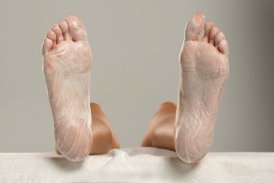 Bare feet soles rubbed with cream absorbed into skin, close-up on gray background, skincare and pedicure moisturizing concept.