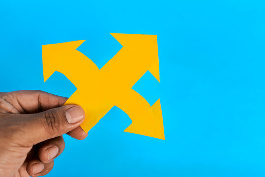 Hand holding yellow three direction paper arrow representing multiple choices on blue background

