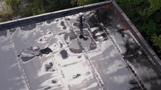 Rain and water damage across industrial commercial business rooftop and flat roof on rubber sealed roofing causing leaks, rainfall tears, and leaking into building exterior from above drone aerial 4k