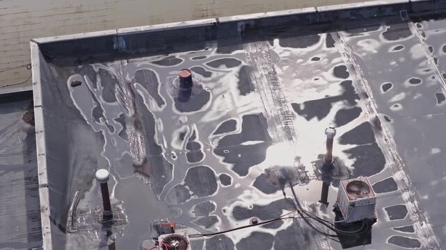 Rain and water damage across industrial commercial business rooftop and flat roof on rubber sealed roofing causing leaks, rainfall tears, and leaking into building exterior from above drone aerial 4k