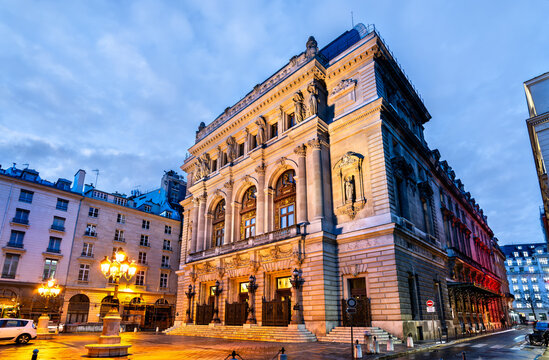 Exterior view of the illuminated classical facade of the Opera Comique theater building at dusk in Paris France.
