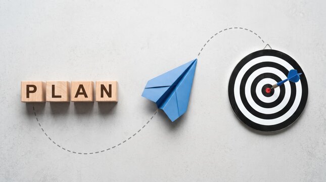 Wooden blocks spelling plan word next to blue paper airplane flying towards target with dart hitting bullseye center representing business strategy goal achievement and success