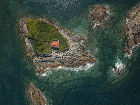 Ermita del Carmen chapel stands on a green island. Surrounded by waves breaking along the rugged shoreline and translucent ocean water. Symbolizing isolation. Faith