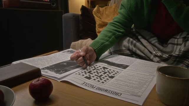 Middle aged man with beard and glasses solving crossword puzzle in newspaper, camera tilting up as he thinks. Footage is perfect for mental wellbeing and cognitive health campaigns