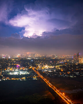 Aerial view of Long Bien Bridge illuminated at night under a dramatic stormy sky with lightning strikes over the city skyline, Hong Ha, Ha Noi, Vietnam.