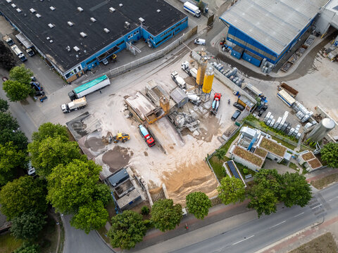 Aerial view of a concrete plant industry with silos, mixing equipment, trucks, and piles of sand in Germany.