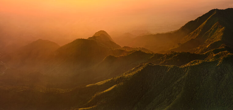 Aerial view of Dieng Plateau with rolling mountain ridges and lush green slopes bathed in warm golden hour light in Indonesia.