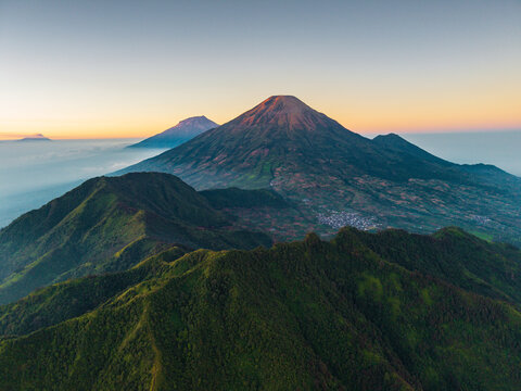 Aerial view of Dieng Plateau with lush green mountain slopes and a small village nestled in the valley under a golden sunrise in Indonesia.