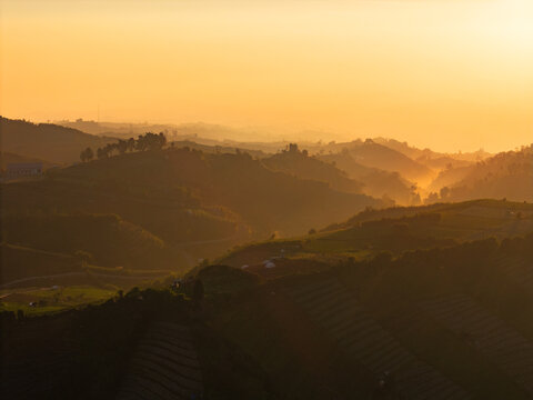 Aerial view of the rolling hills and terraced fields of the Dieng Plateau bathed in golden hour light in Indonesia.