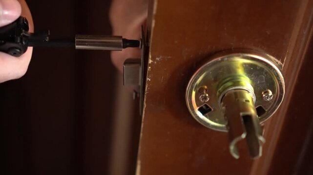 Close-up of hands installing a door lock using a multipurpose hand tool. The tool is aligned with precision, showing skillful craftsmanship in a residential setting