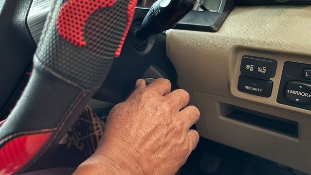 Detailed view of automobile dashboard showing steering wheel with red-black cover and hand pressing dashboard switches. Represents automotive interior, manual operation, and driving safety.