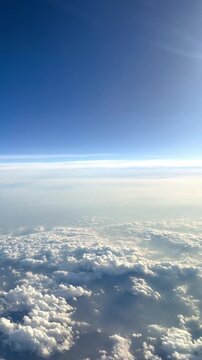 Aerial View Above Clouds from Airplane. Aerial view above white clouds and blue sky during flight. Peaceful sky background from airplane window.
