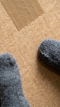 Hands holding cardboard box with feet in gray socks on wooden floor with box
