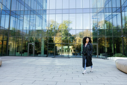 Black woman going and looking at camera near glass skyscraper building