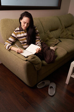 Woman writing in notebook while sitting on couch