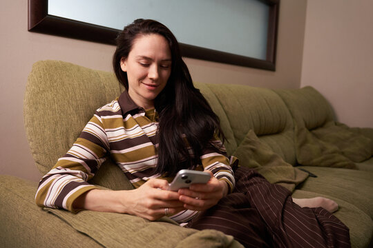 Woman uses smartphone while relaxing on couch