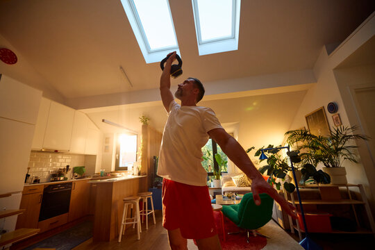 A man works out in the living room, holding a kettlebell.