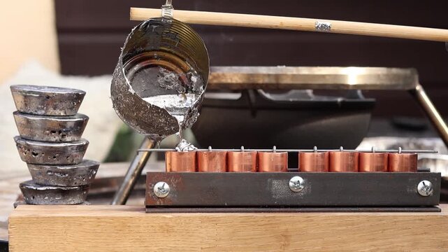 Close up of pouring liquid molten lead into small molds with a tin can attached to a wooden handle. Crafting lead fishing weights and sinkers using recycled materials.