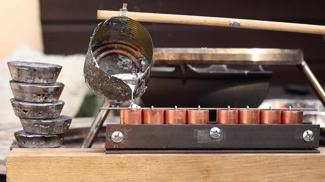 Close up of pouring molten lead scrap using a homemade tin can ladle attached to a wooden stick. Concept of DIY casting, metal recycling, and home workshop process.