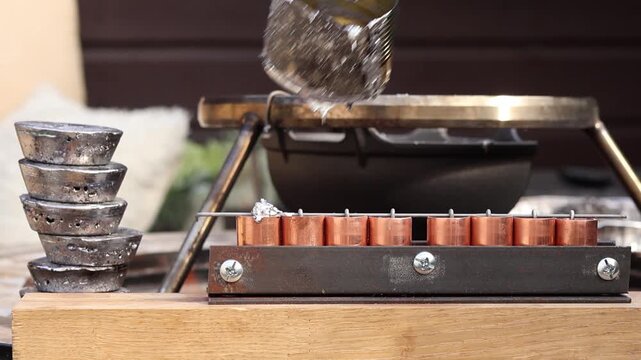 Man hand pouring molten lead into custom molds with a tin can ladle on a wooden stick, then moving it away to refill. Process of making handmade fishing sinkers in a home workshop.