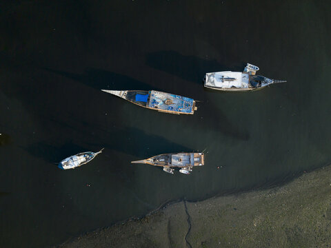 Aerial view of traditional wooden boats anchored in the calm waters of Bali Nature Harbour, with a sandy shoreline in Kecamatan Denpasar Selatan, Bali, Indonesia.