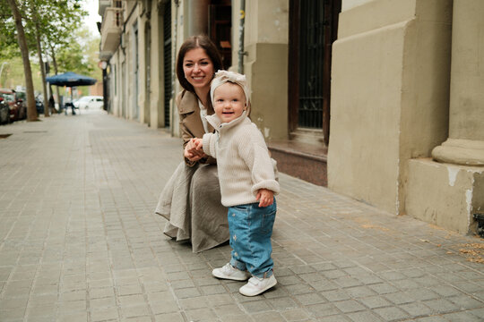 Happy mother holding her baby girl by the hand in the street 
