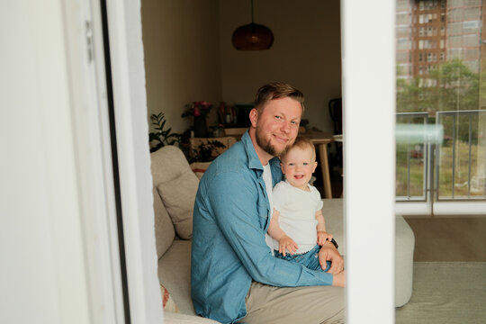 Happy smiling father and his little baby girl at home sitting on couch