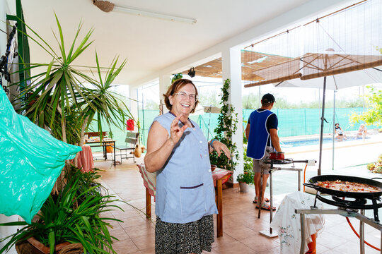Senior woman smiling preparing paella outdoors by pool
