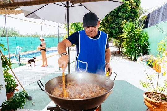 Man cooking paella outdoors near swimming pool