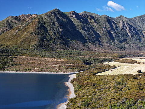 Aerial view of the deep blue waters of Lake Coleridge bordered by dense native forest and steep mountain slopes in Lake Coleridge, Canterbury Region, New Zealand.