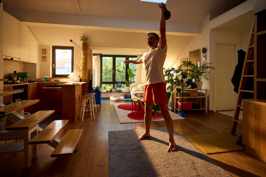 Man exercises in the living room with a kettlebell