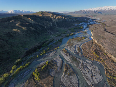 Aerial view of Clay Cliffs with rugged rock formations and a braided river winding through the landscape in Omarama, Canterbury Region, New Zealand.