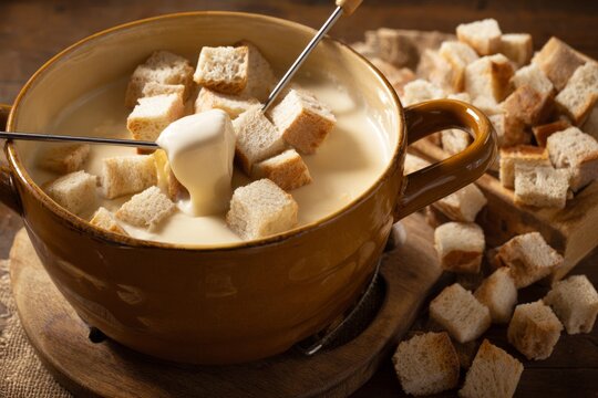 Ceramic cheese fondue pot on wooden trivet with bread cubes, cheese fondue dinner concept
