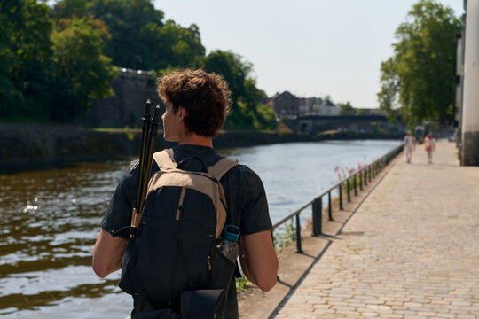 Walking Along the River With a Backpack and Tripod in the Sun
