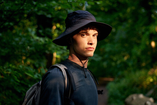 Young Man Stands on a Forest Path Wearing a Hat and Backpack