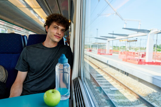 Young Man Sits by Window on Train During Daytime Journey