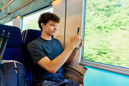 A Young Man Sits on a Train, Focused on His Phone