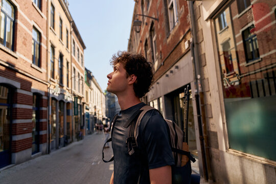 Young Man Walks in City Street Looking up at Buildings