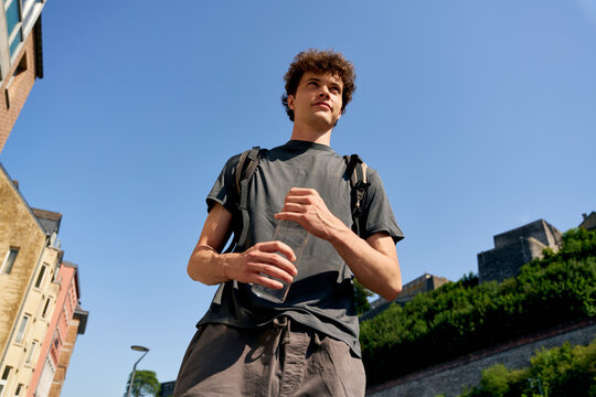 Young Man Holds Water Bottle on Sunny Street During Day