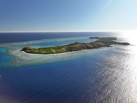 Aerial view of Mana Island surrounded by turquoise coral reefs and deep blue ocean waters in Western Division, Fiji.