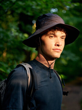 Young Man Walks in Forest Wearing Hat and Backpack During Daytime