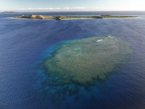 Aerial view of Mana Island surrounded by a vibrant coral reef in the deep blue ocean of the Western Division, Fiji.