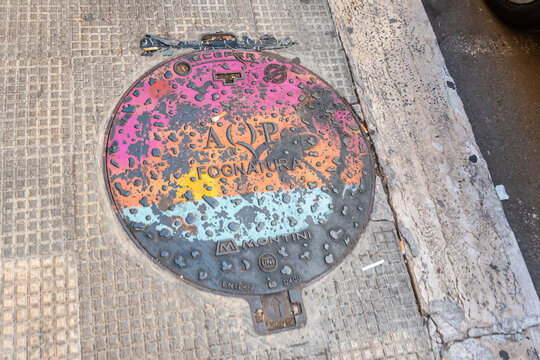 Bari, Italy - June 31, 2026: Colorful painted manhole cover with AQP Fognatura sewage system inscription and Montini manufacturer marking on sidewalk pavement