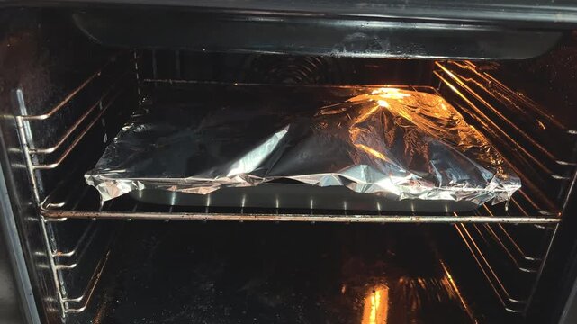Roasted turkey thigh with small new potatoes on a baking sheet under foil, home cooking, hearty dinner, baked food.