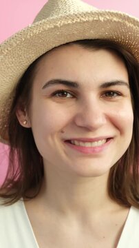 Vertical video of young beautiful happy brunette woman in straw hat smiling on the pink background